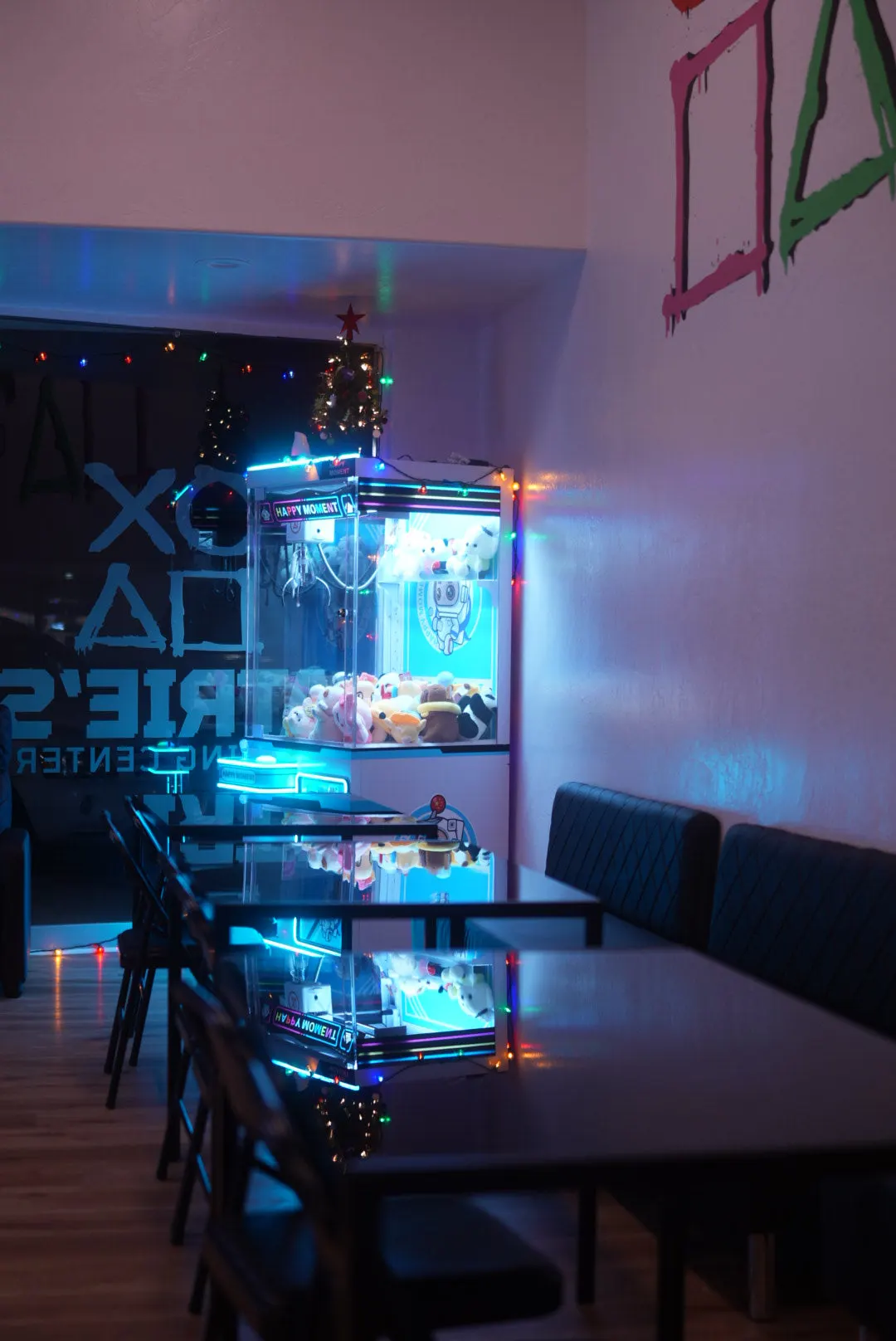 Tabletop gaming tables and booth seating lit by a claw machine