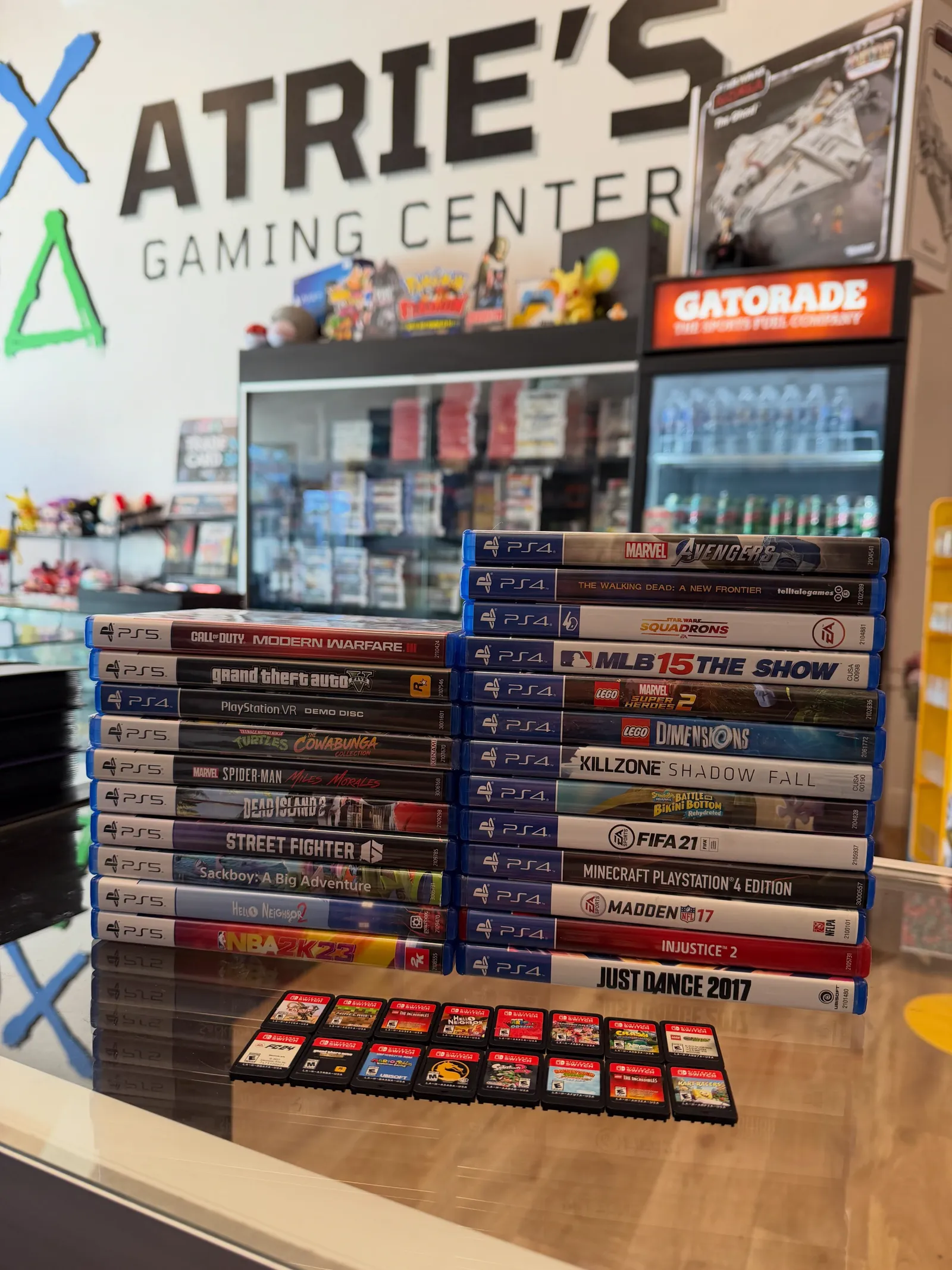 Stacks of traded-in PlayStation 4 and Nintendo Switch games on the counter in front of the Atrie's logo wall